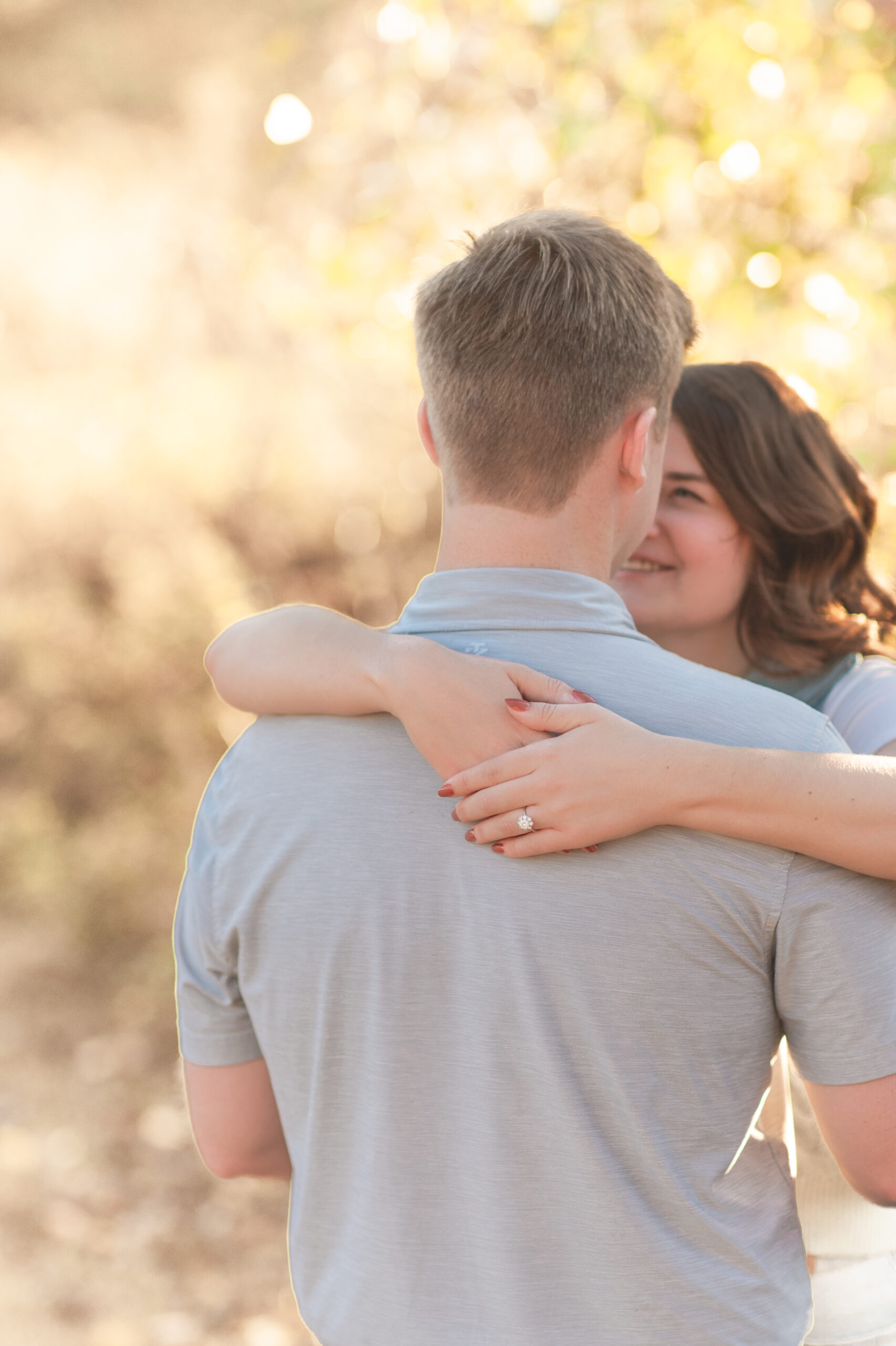 Woman has arms wrapped around neck of man, showcasing engagement ring