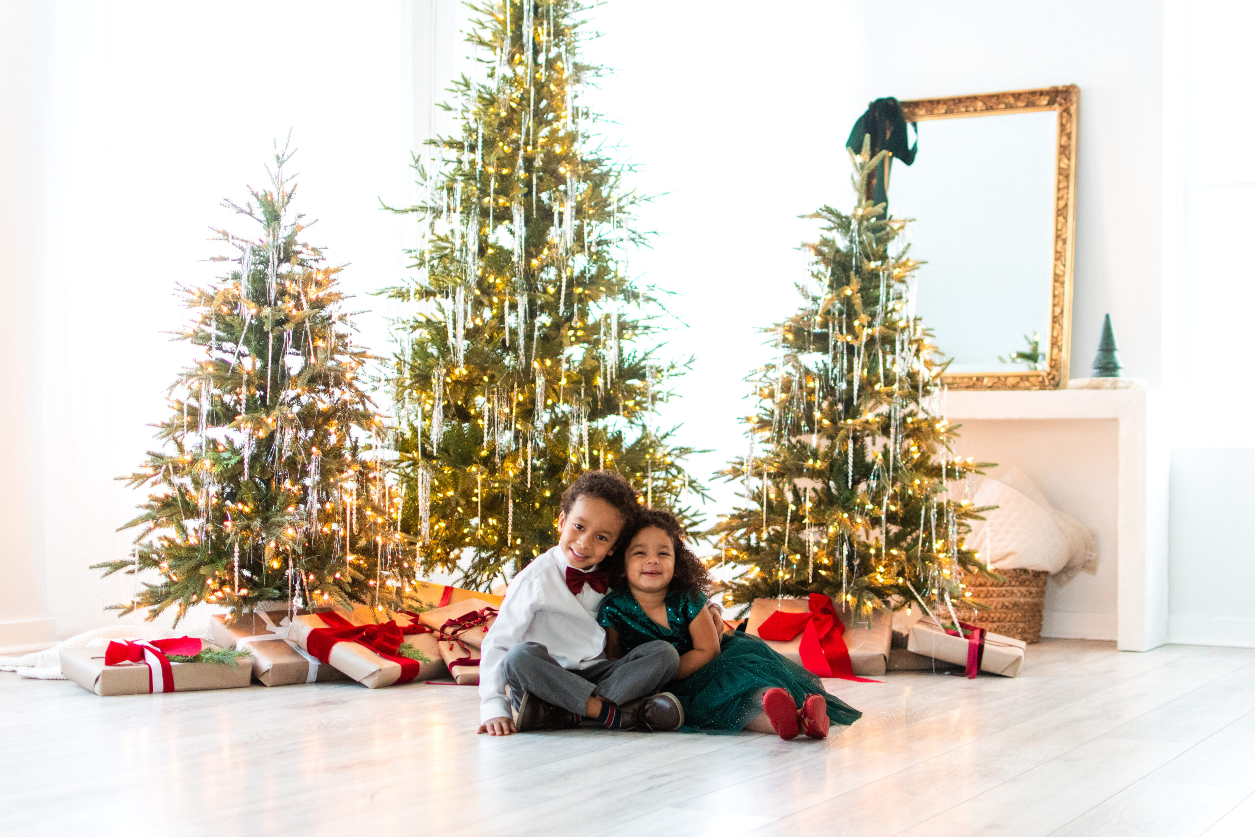 Brother and sister sitting side by side in front of Christmas trees