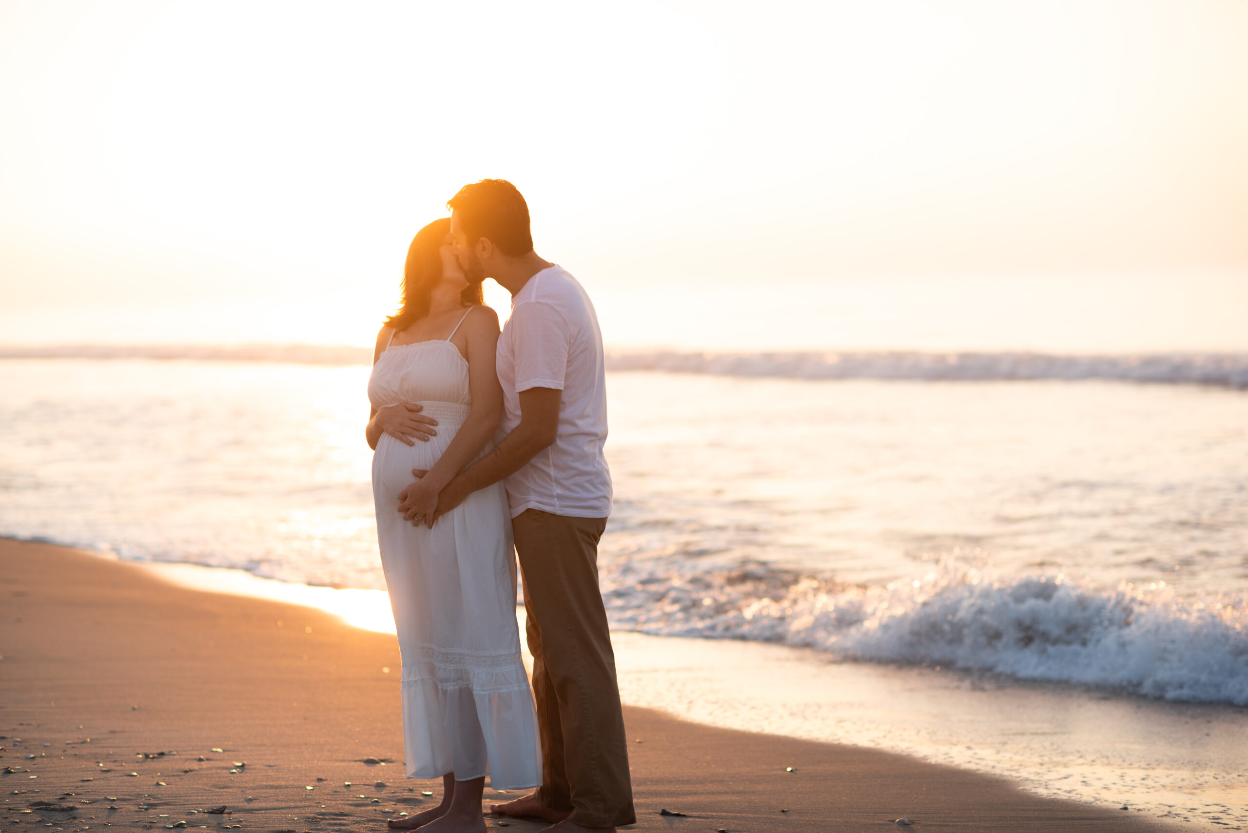 An expecting couples is posing at the beach at sunrise for their maternity session.